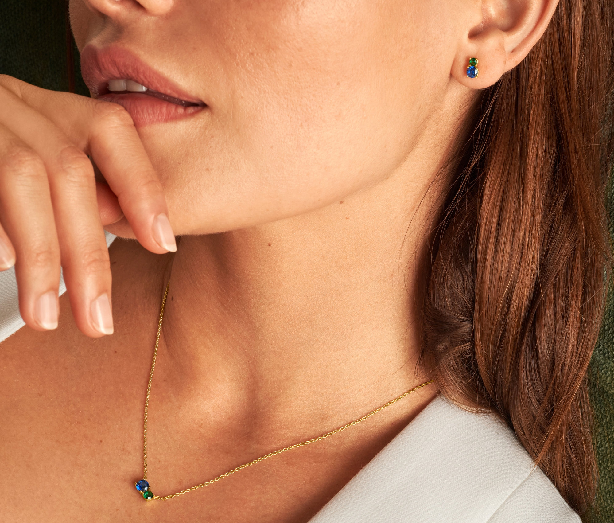 Detail ženy s prstom pri ústach, ktorá má na sebe striebornú modrozelenú retiazku a strieborné modrozelené napichovacie náušnice s rýdzosťou 925.