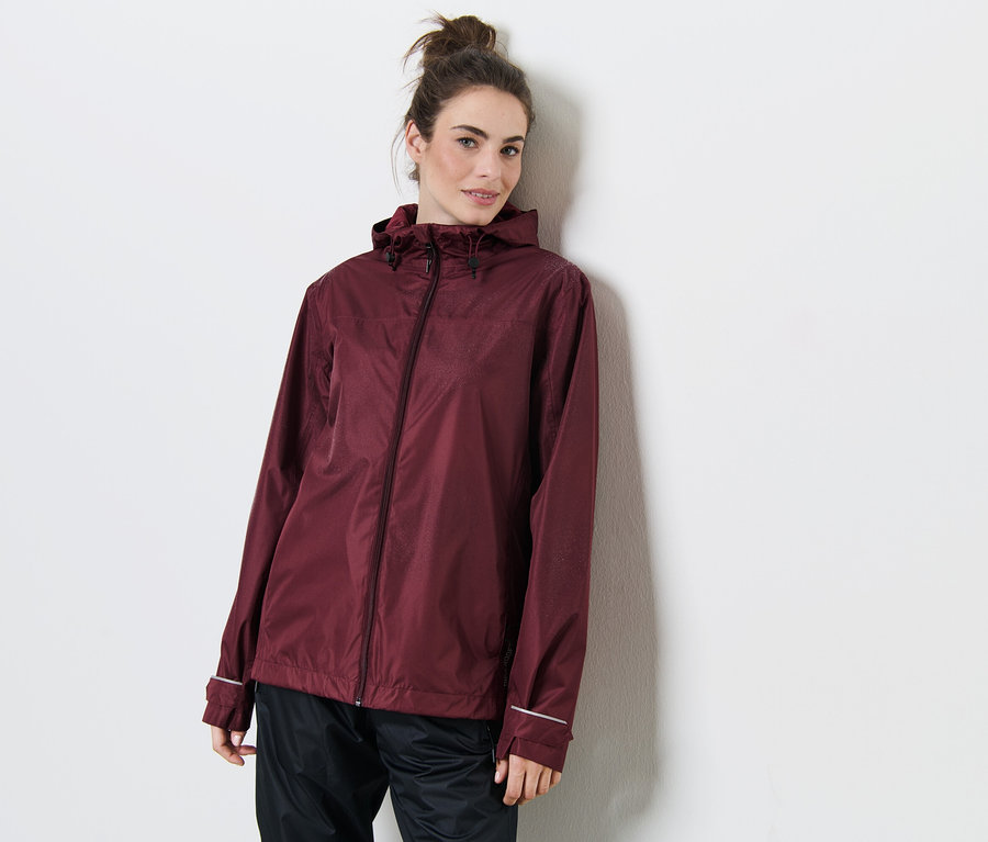 Žena opretá o stenu má na sebe vínovočervenú bundu do dažďa.