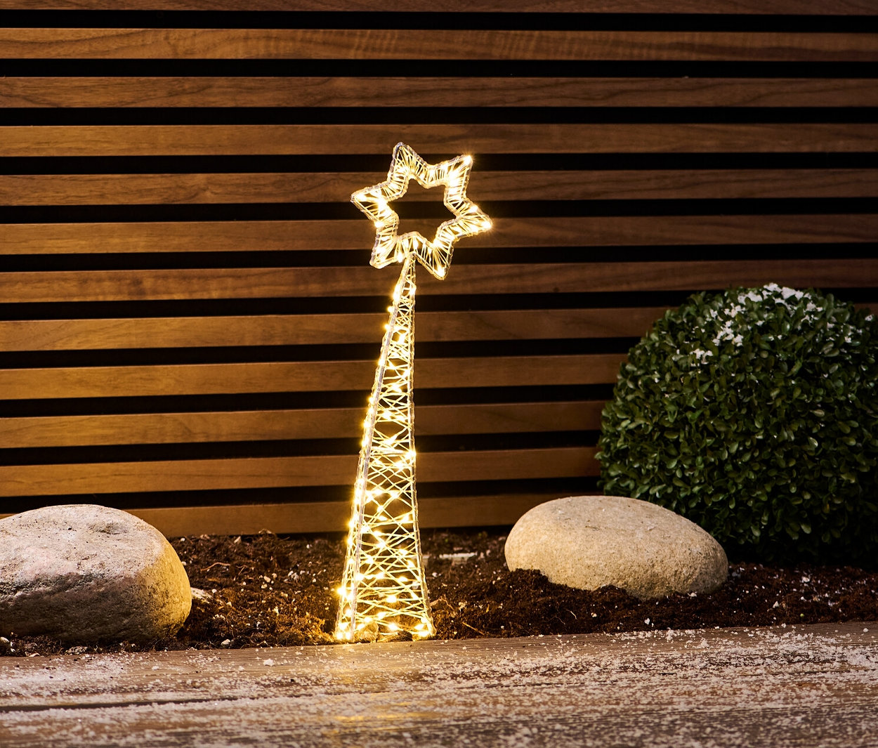 Malá LED padajúca hviezda stojí medzi kameňmi a kríkom.