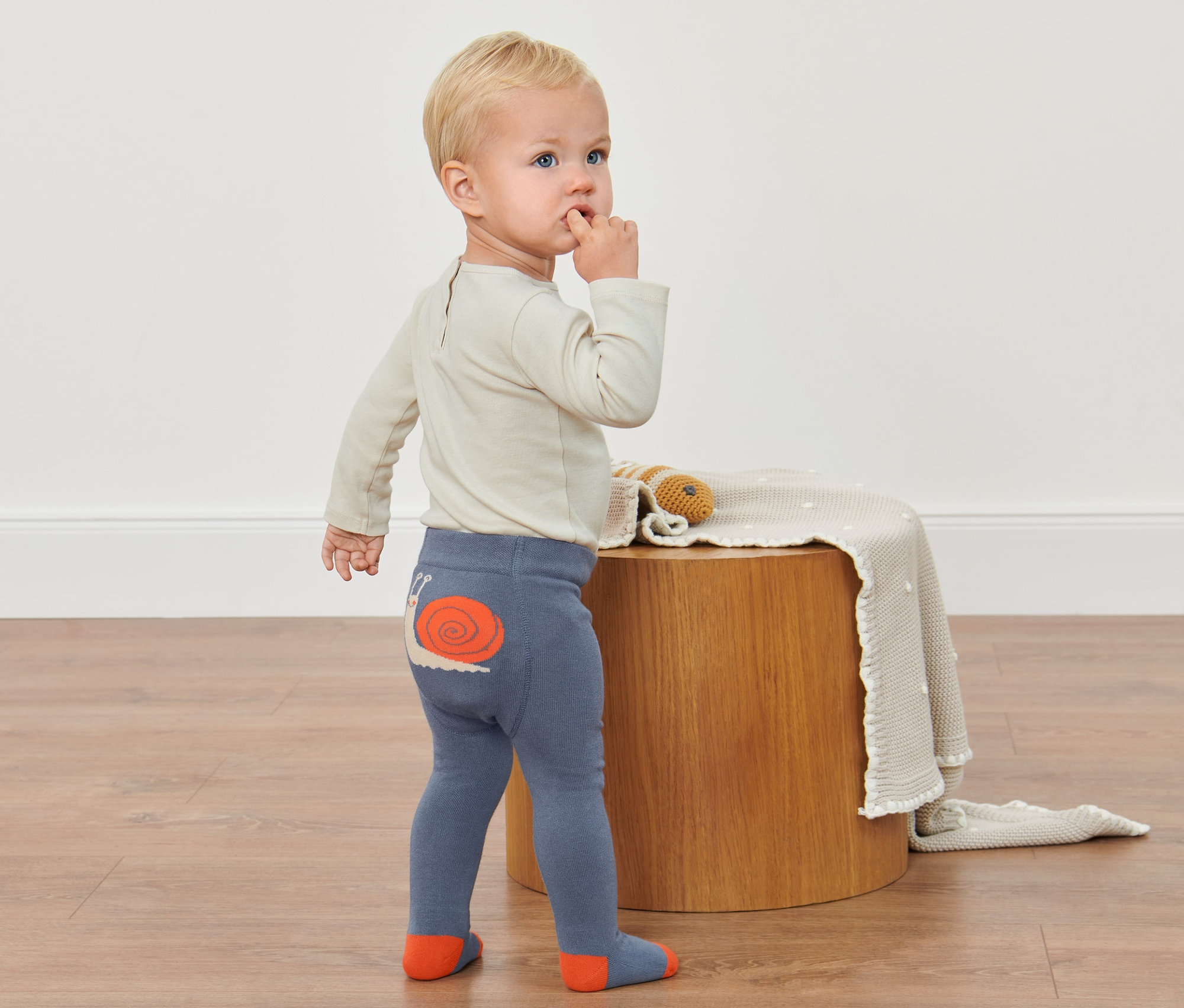 Batoľa stojí na podlahe a má na sebe pančuchy so slimákom.