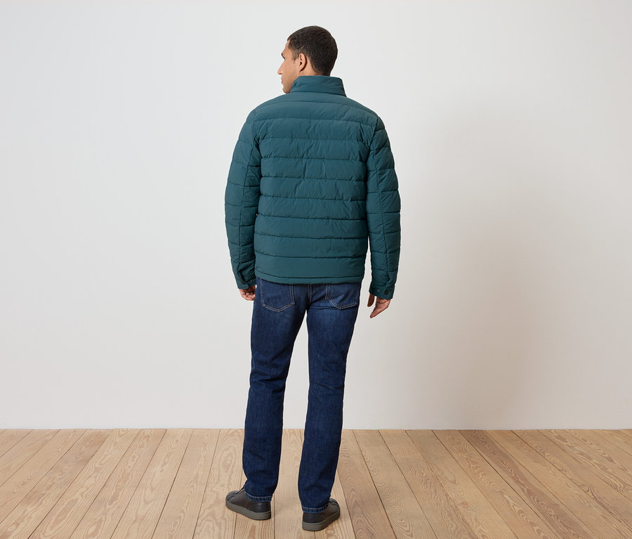 Muž chrbtom k fotoaparátu má na sebe zelenú páperovú bundu, džínsy a topánky.