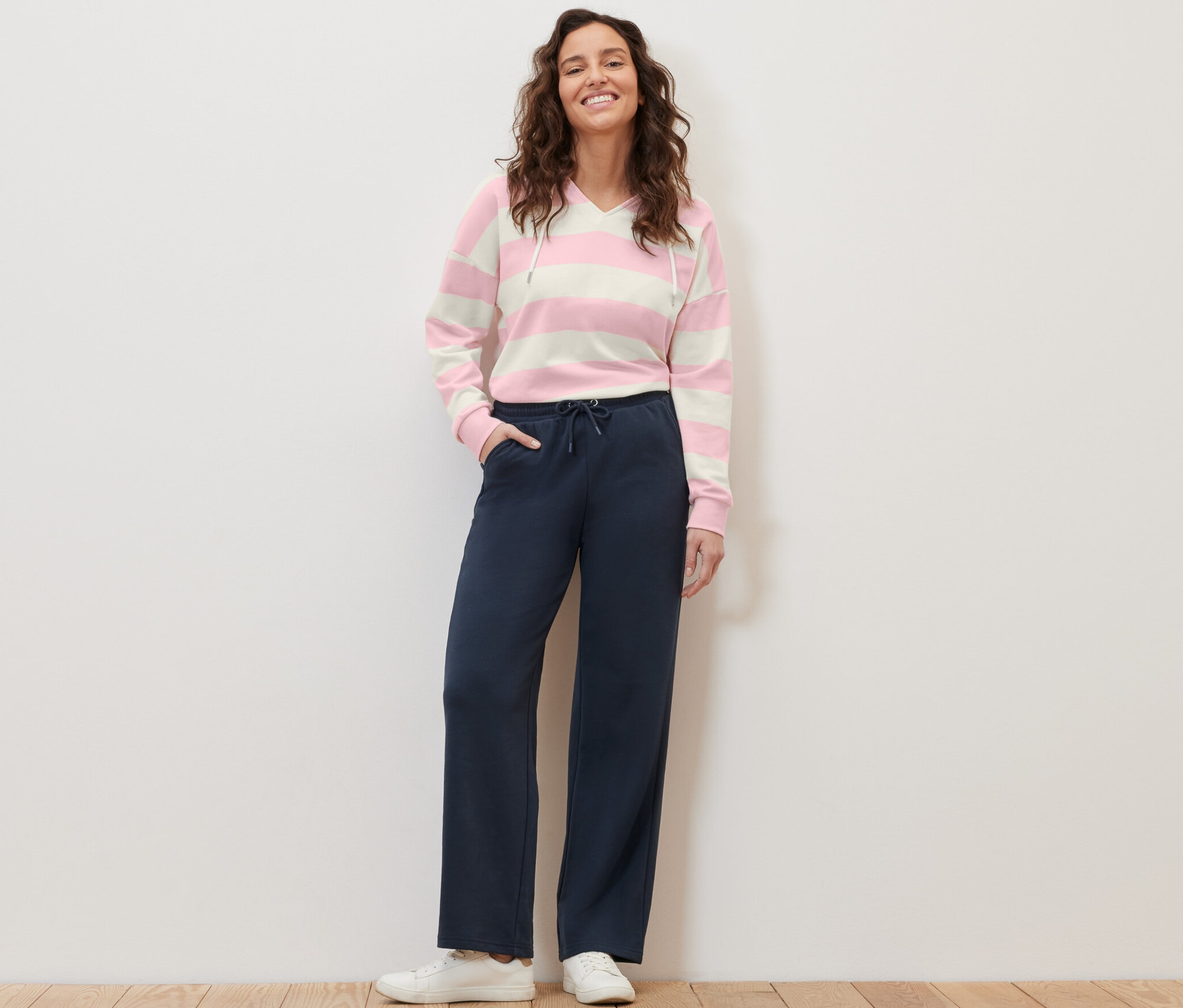 Žena stojí a pózuje v tmavomodrých teplákoch a pruhovanom svetri s kapucňou.