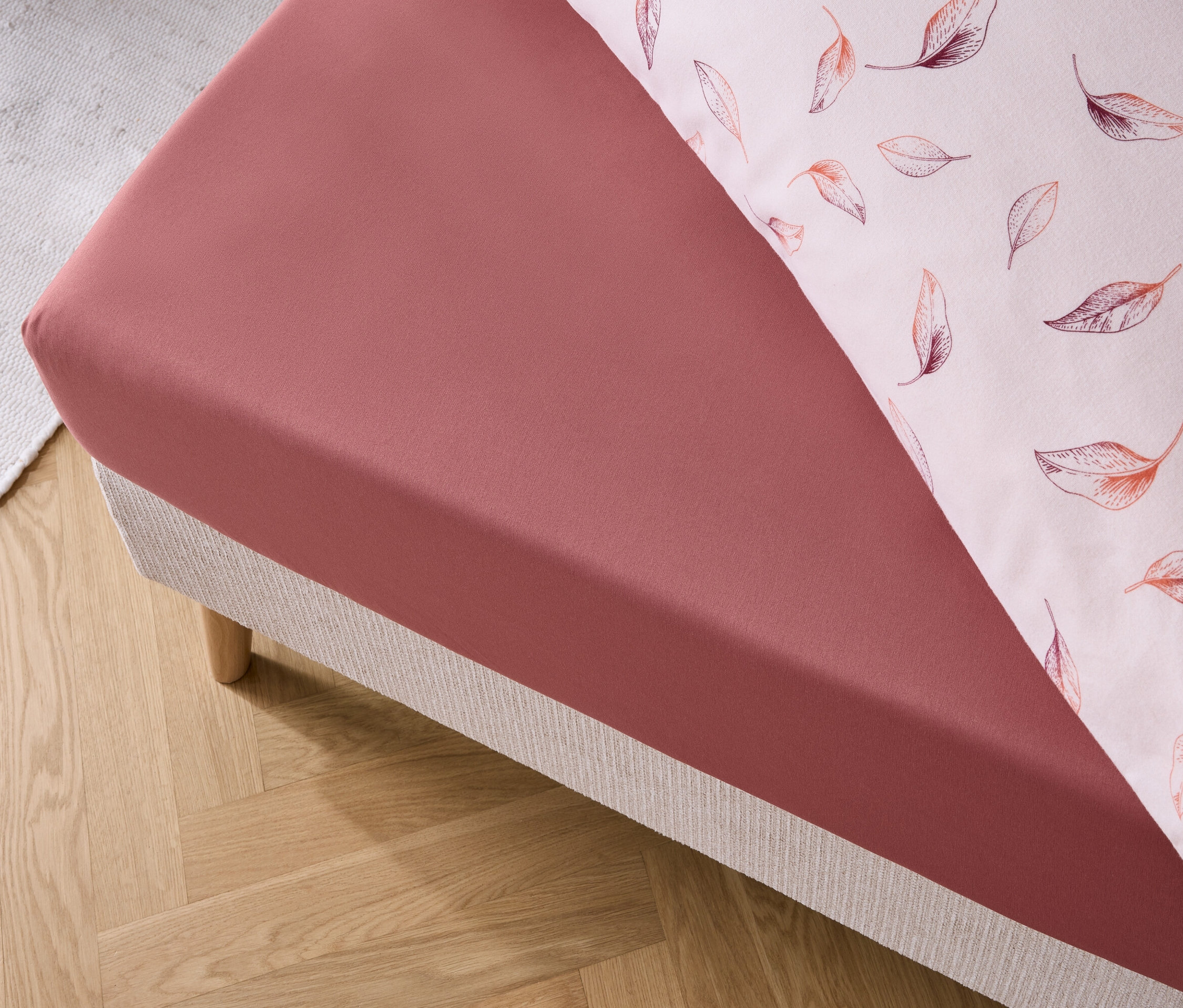 Detail červenej plachty a obliečky na vankúš s potlačou listov na posteli.