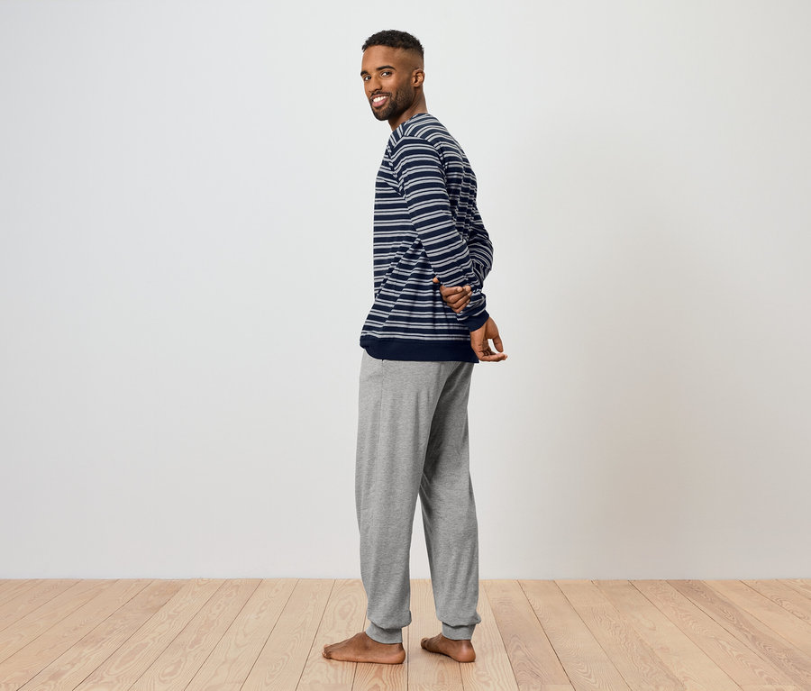 Muž sa pozerá cez plece a usmieva sa. Má na sebe pruhované tričko a sivé tepláky.