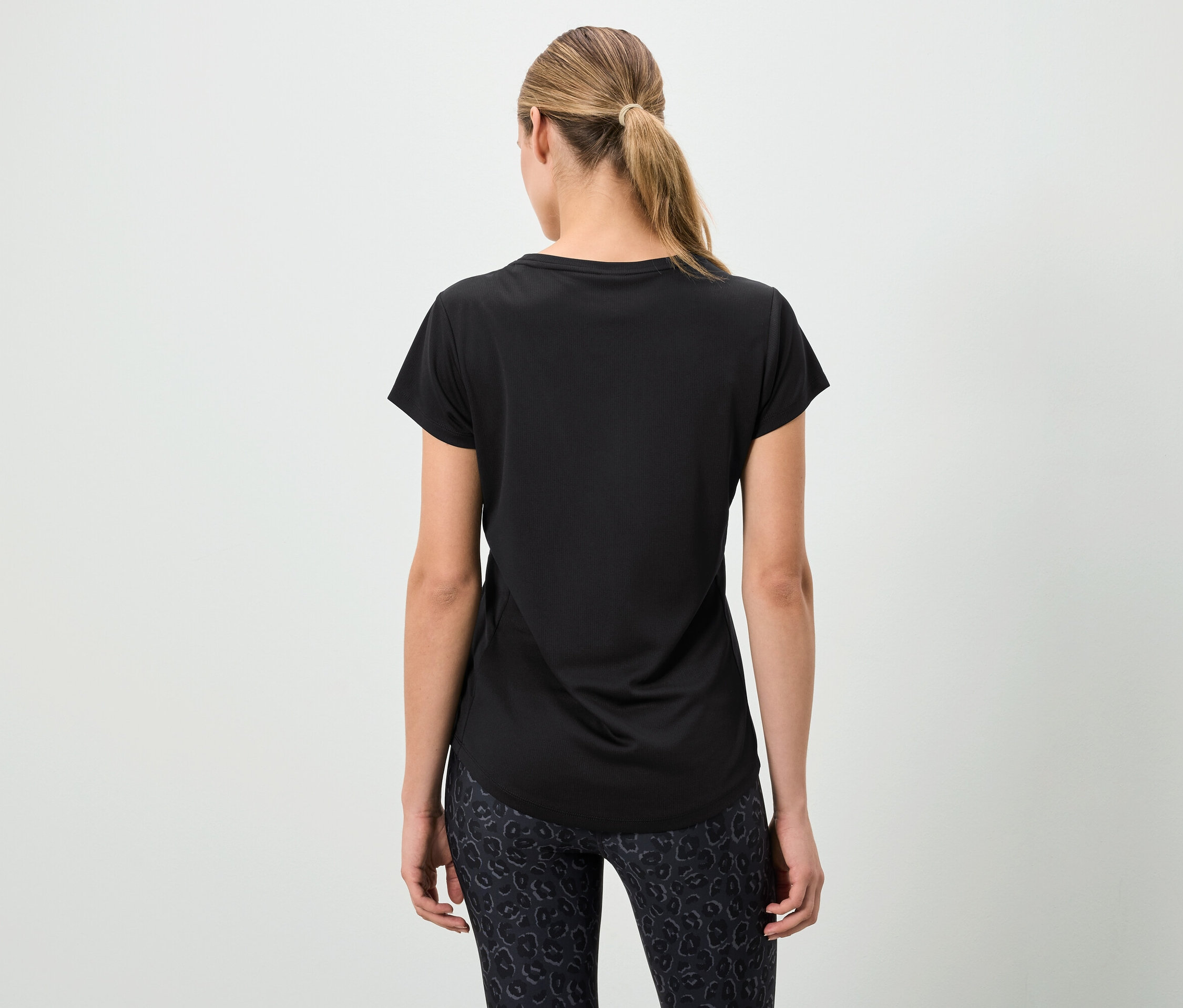 Žena chrbtom k fotoaparátu má na sebe čierne tričko a vzorované legíny.