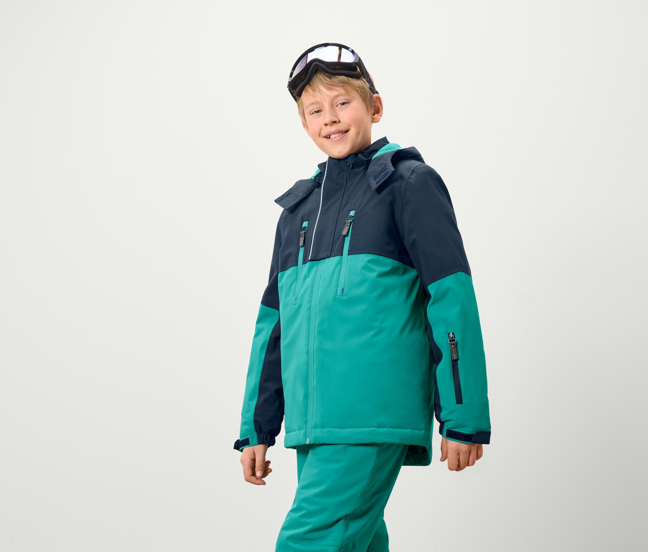 Chlapec v lyžiarskej bunde a nohaviciach, s lyžiarskymi okuliarmi na hlave.