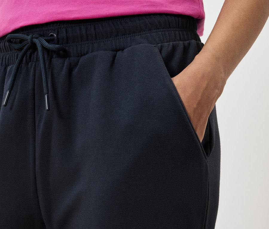 Detailný pohľad na tmavomodré tepláky s rukou vo vrecku a ružovým tričkom.