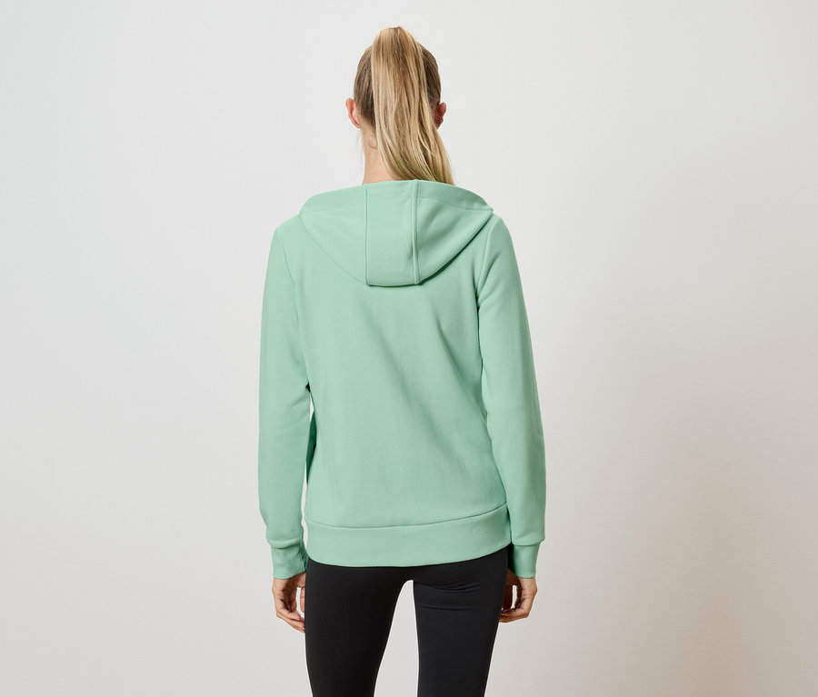 Pohľad zozadu na ženu s blond vlasmi zopnutými do copu, ktorá má na sebe svetlozelenú mikinu s kapucňou a čierne legíny.