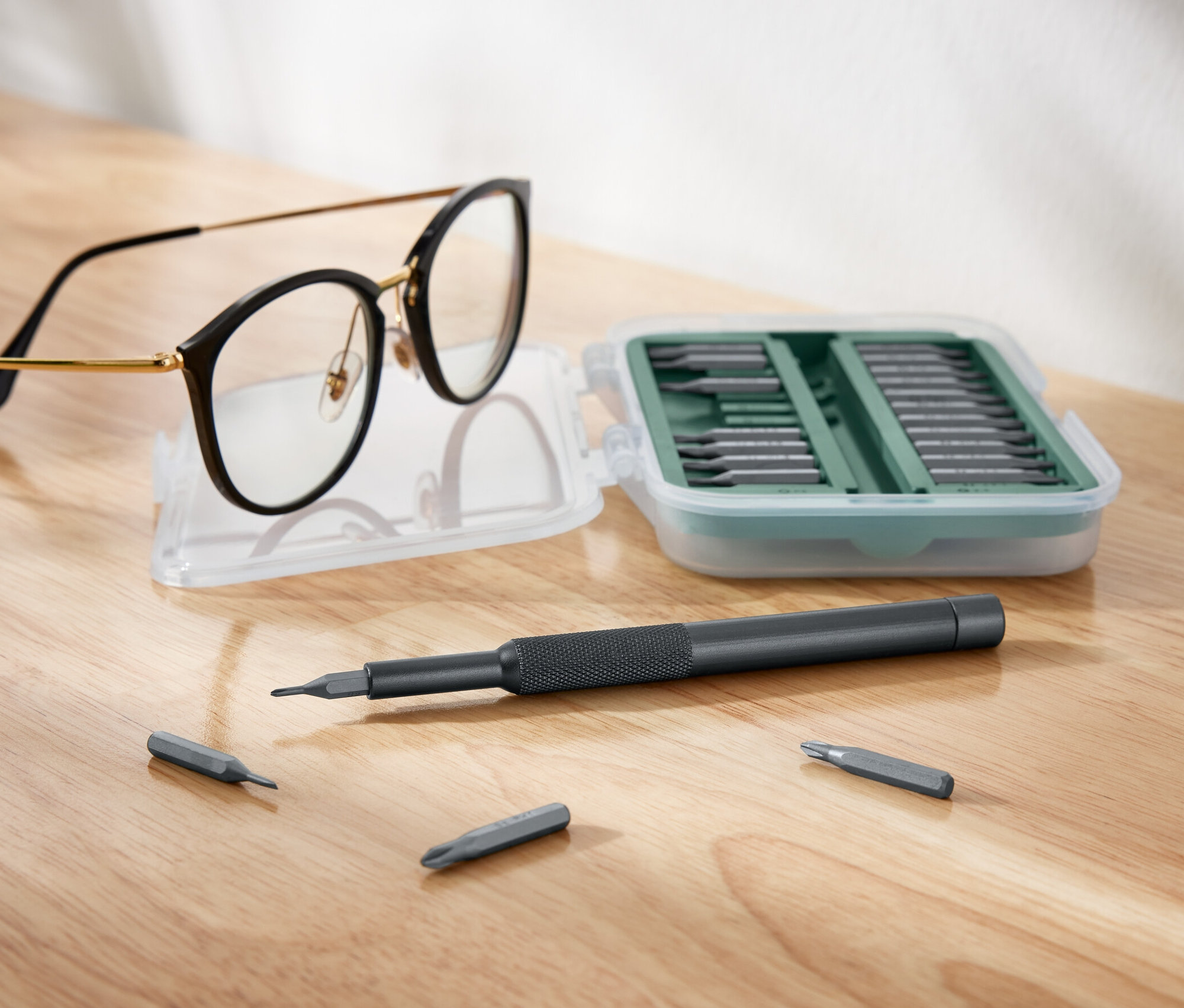 Okuliare ležia vedľa otvorenej sady skrutkovačov.