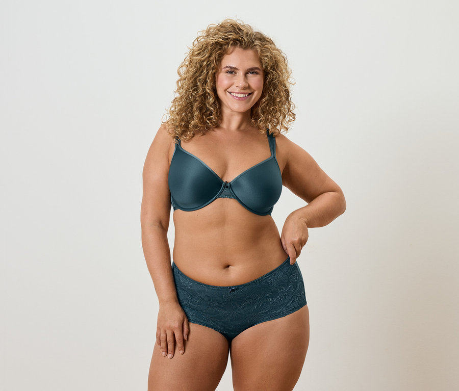 Žena s kučeravými blond vlasmi v petrolejovej podprsenke a ladiacej spodnej bielizni.