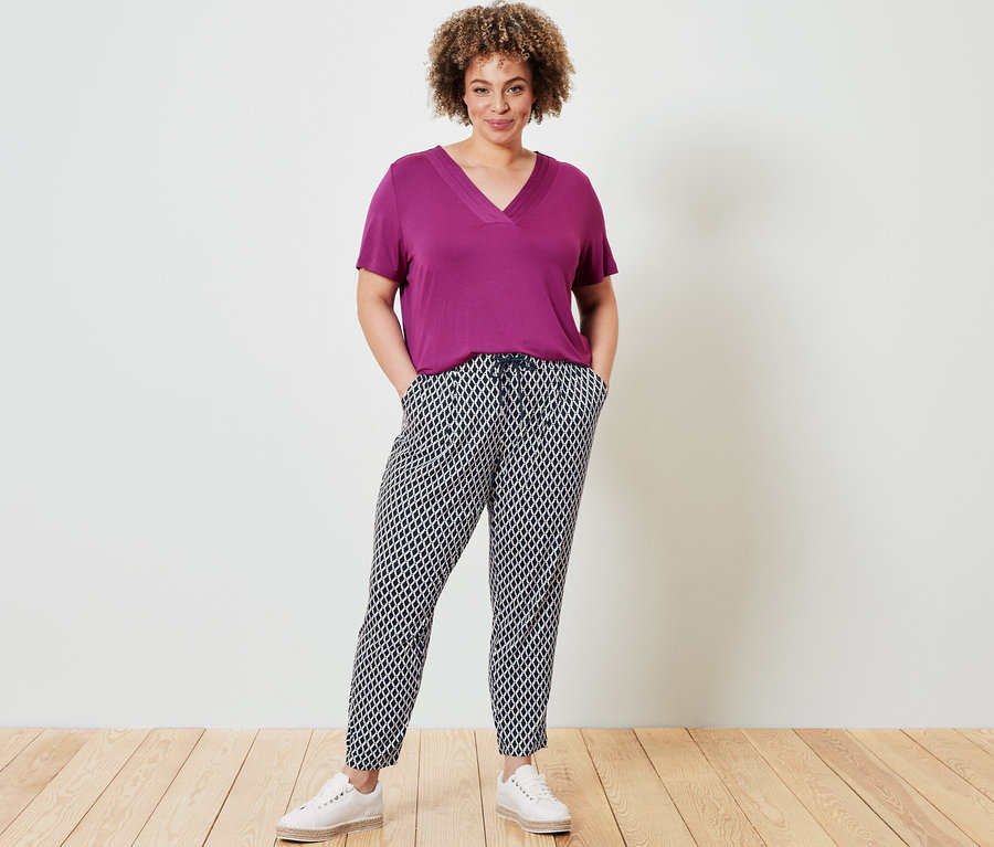 Žena pózuje v tričku so záhybom, bordové a v džersejových nohaviciach s potlačou.