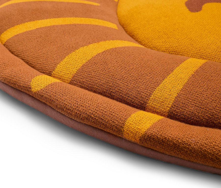 Detailný pohľad na okrúhly hnedý vankúš so žltými pruhmi.