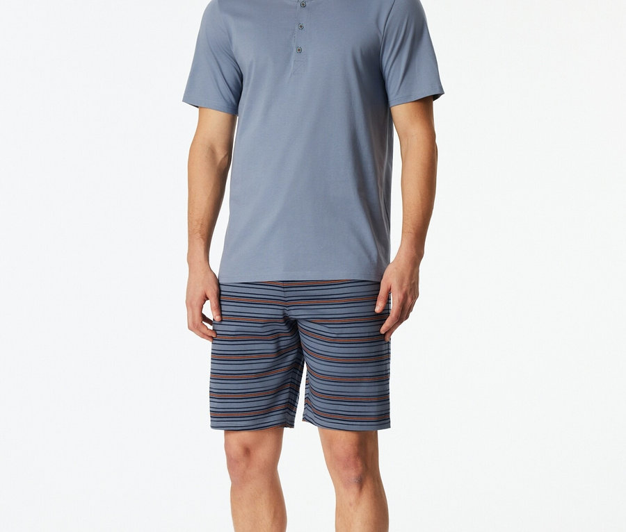 Muž v modrom pyžamovom tope s gombíkmi a pruhovaných šortkách.