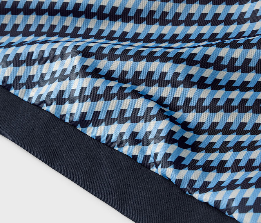 Detail látky s modrým, svetlomodrým a bielym geometrickým vzorom a tmavomodrým lemom.