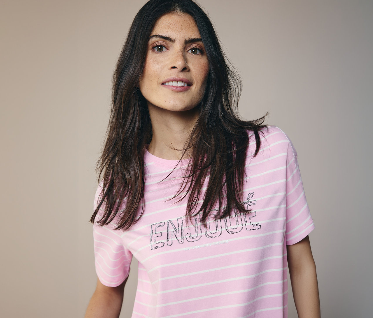 Žena s dlhými tmavými vlasmi má na sebe tričko CECIL s ružovo-bielymi pruhmi a nápisom 'ENJOUE'.