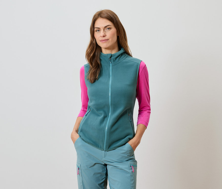 Žena v petrolejovej veste a zladených nohaviciach s ružovým tričkom s dlhým rukávom.