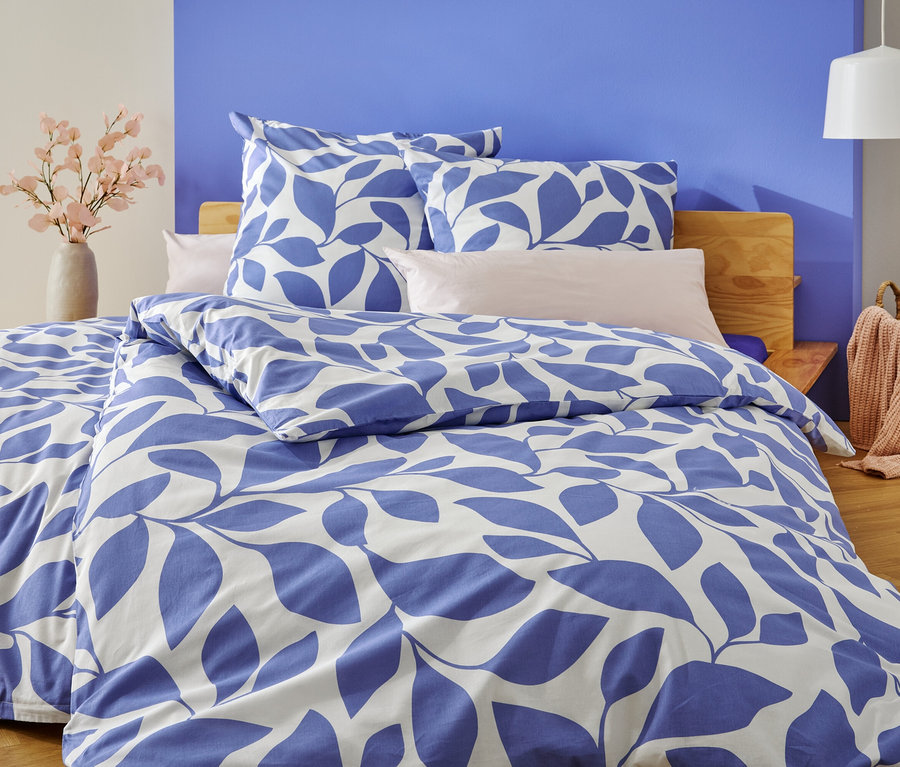 Posteľ s modro-bielou posteľnou bielizňou s listami stojí pred modro-bielo natretou stenou.