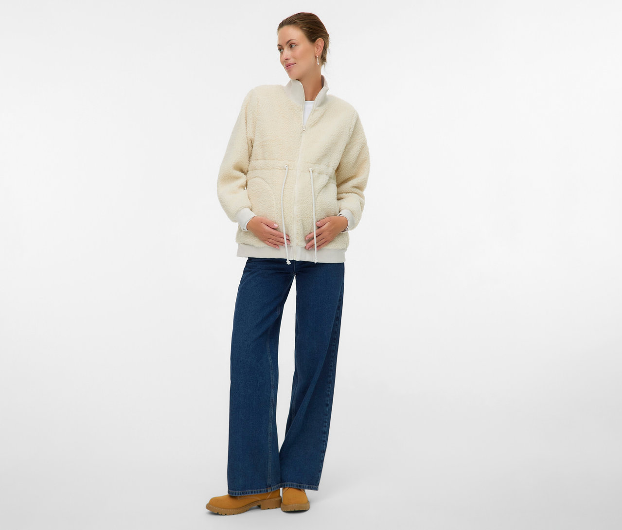 Tehotná žena má na sebe plyšovú bundu MAMALICIOUS 3 v 1 »MLCARLY«, džínsy a členkové topánky.