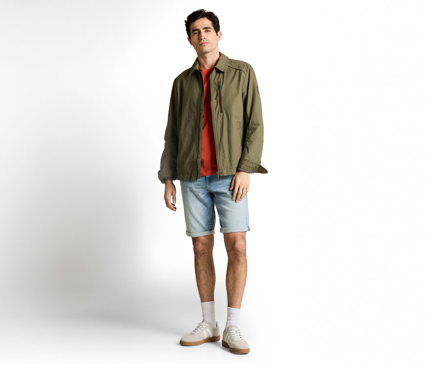 Muž v olivovozelenej bunde a Tom Tailor TTJOSH REGULAR SLIM Jeans Shorts, light stone blue denim, k tomu tričko, ponožky a tenisky.