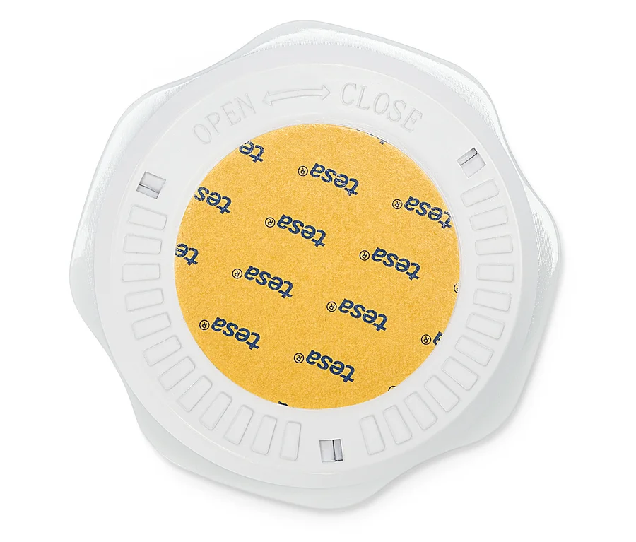 Pohľad zhora na okrúhlu, bielu škatuľku na lepiacu pásku Tesa so žltou lepiacou páskou, na ktorej je vytlačené logo Tesa.