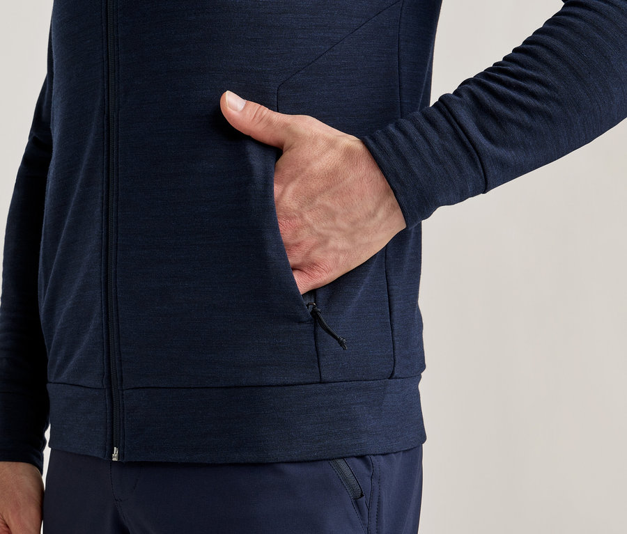 Detail osoby v tmavomodrej bunde na zips s rukou vo vrecku.