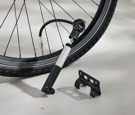 Pneumatika bicykla je hustená striebornou pumpou s čiernou rukoväťou a analógovým manometrom. Vedľa na zemi leží čierna konzola.