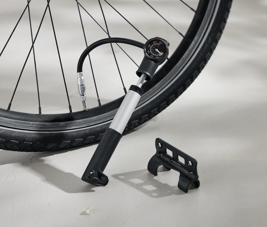 Pneumatika bicykla je hustená striebornou pumpou s čiernou rukoväťou a analógovým manometrom. Vedľa na zemi leží čierna konzola.