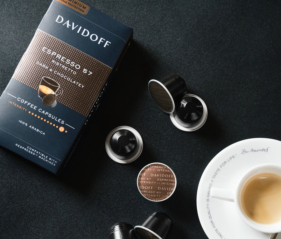 Balenie a niekoľko kapsúl DAVIDOFF CAFÉ Espresso 57 Ristretto vedľa šálky espressa na čiernom pozadí.