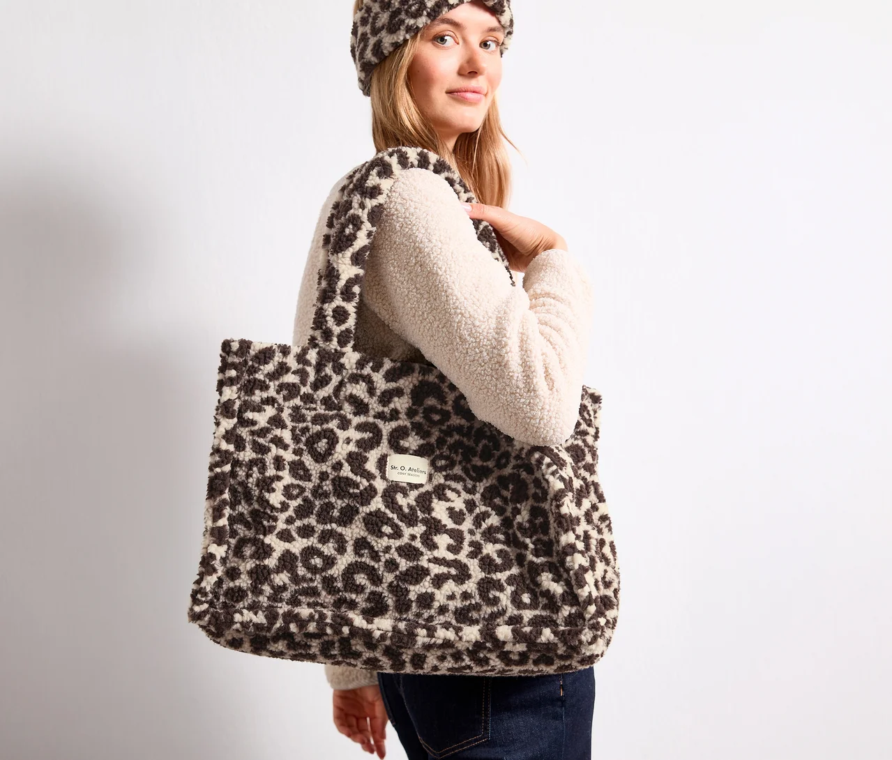 Blondínka nesie na ramene chlpatú nákupnú tašku Street One s leopardím vzorom a má na sebe zladenú čelenku.