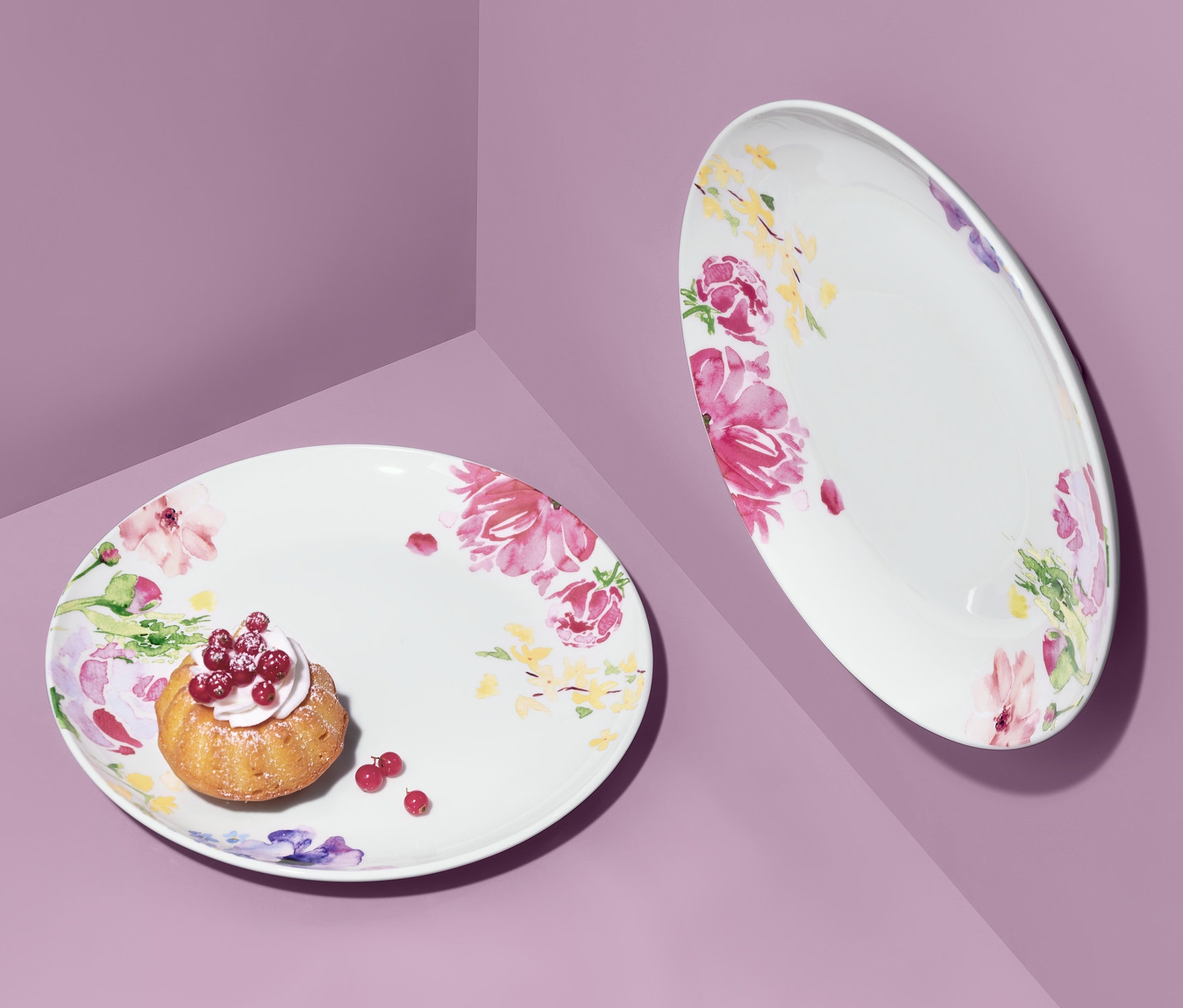 Dva taniere s kvetinovým vzorom na fialovom pozadí. Na jednom tanieri je malý koláčik s ovocím.