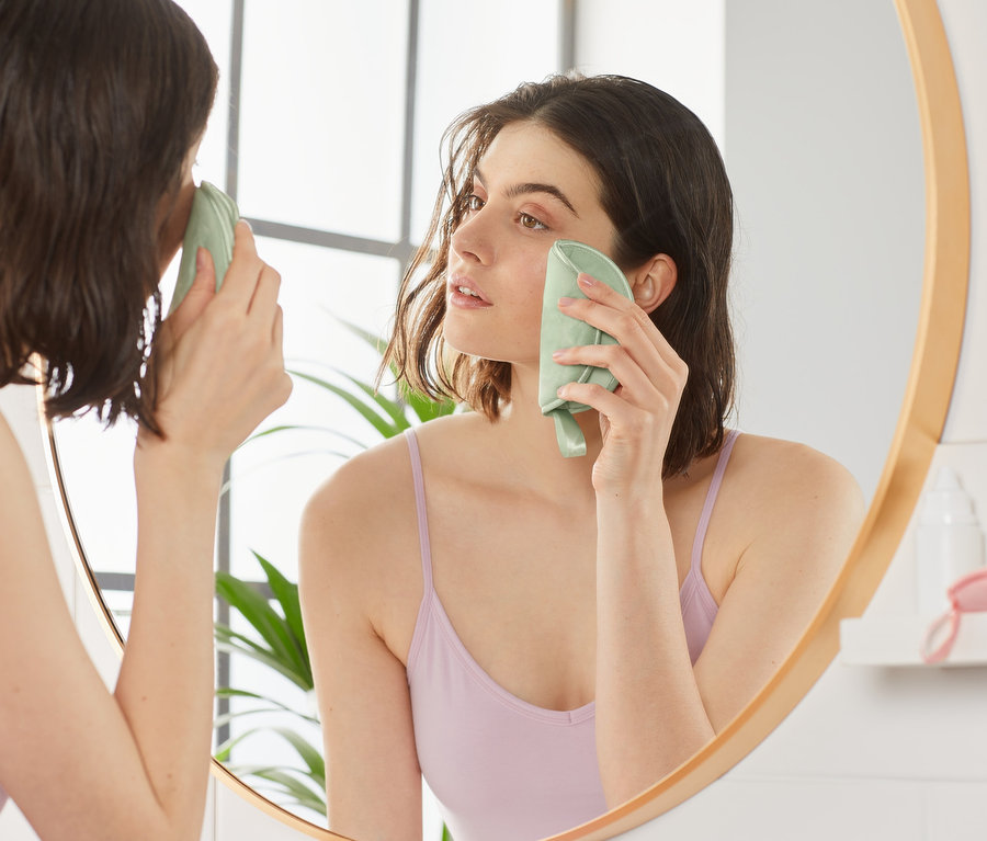 Žena si odličuje make-up z tváre pomocou obzvlášť veľkého odličovacieho tampónu na opakované použitie, 3 ks, a pozerá sa do zrkadla.