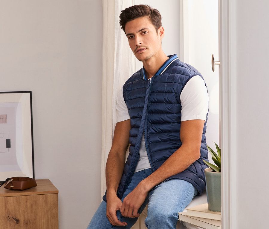 Muž sedí na parapete v modrej prešívanej veste.