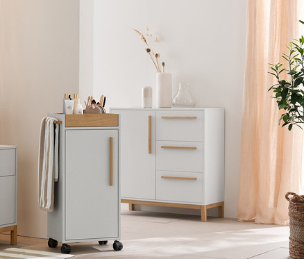 Svetlosivá kúpeľňa s vysokou skrinkou »Eklund«, skrinkou pod umývadlo so zásuvkami a odkladacou skrinkou. Ďalej béžovo-biele uteráky, predložka a úložné košíky.