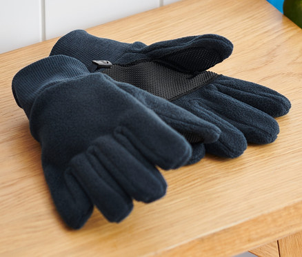 Na drevenej lavici ležia detské flísové rukavice vedľa batohu a skateboardu.