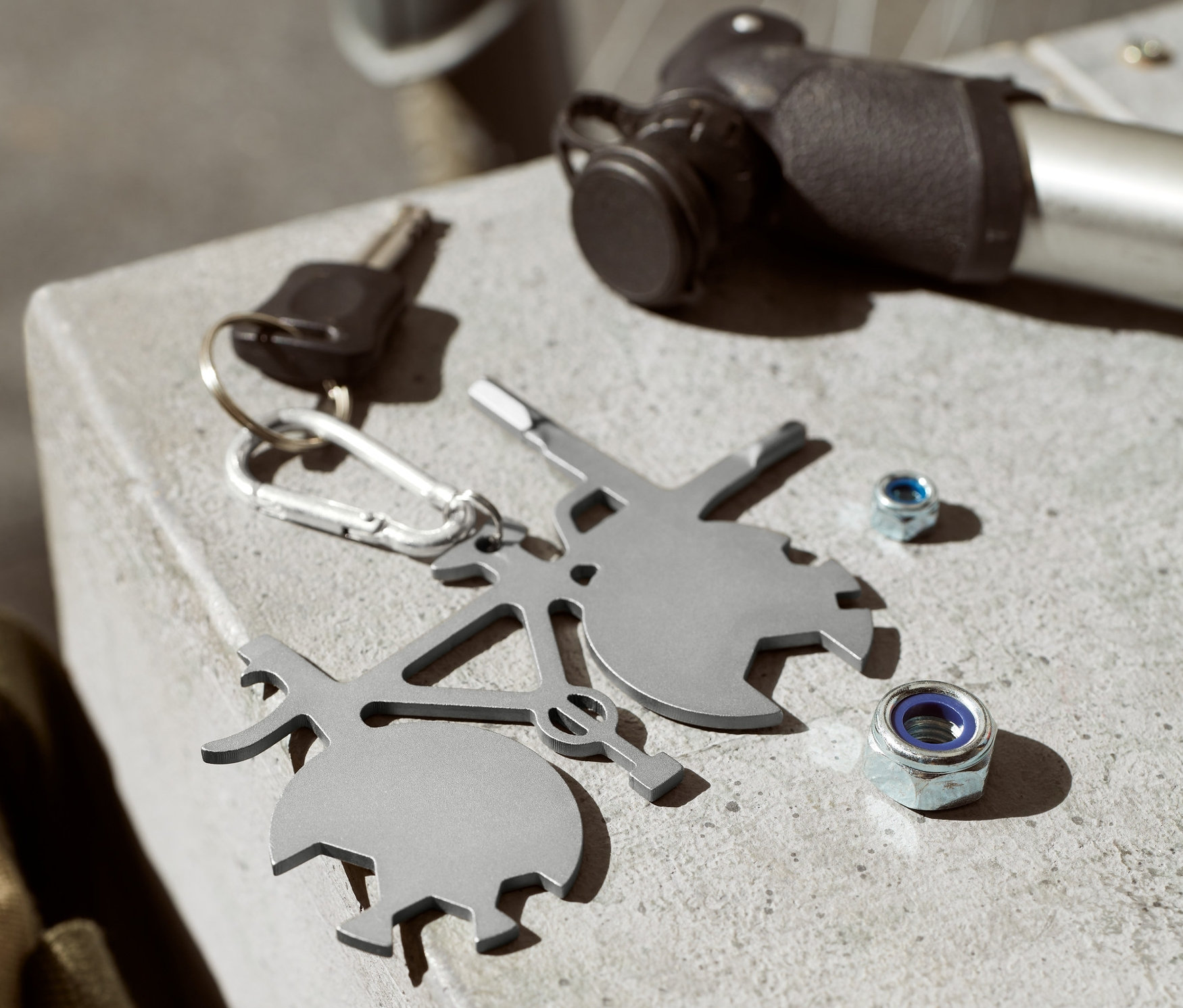 Na betónovom povrchu leží multifunkčný nástroj na bicykel, kľúč, hustilka a dve skrutky.