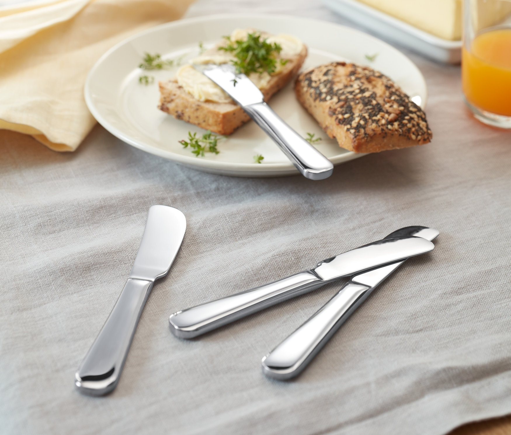 Na stole leží chlieb s maslom a 4 nože na maslo.