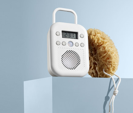 Na modrom podstavci stojí biele rádio do kúpeľne a prírodná umývacia huba.
