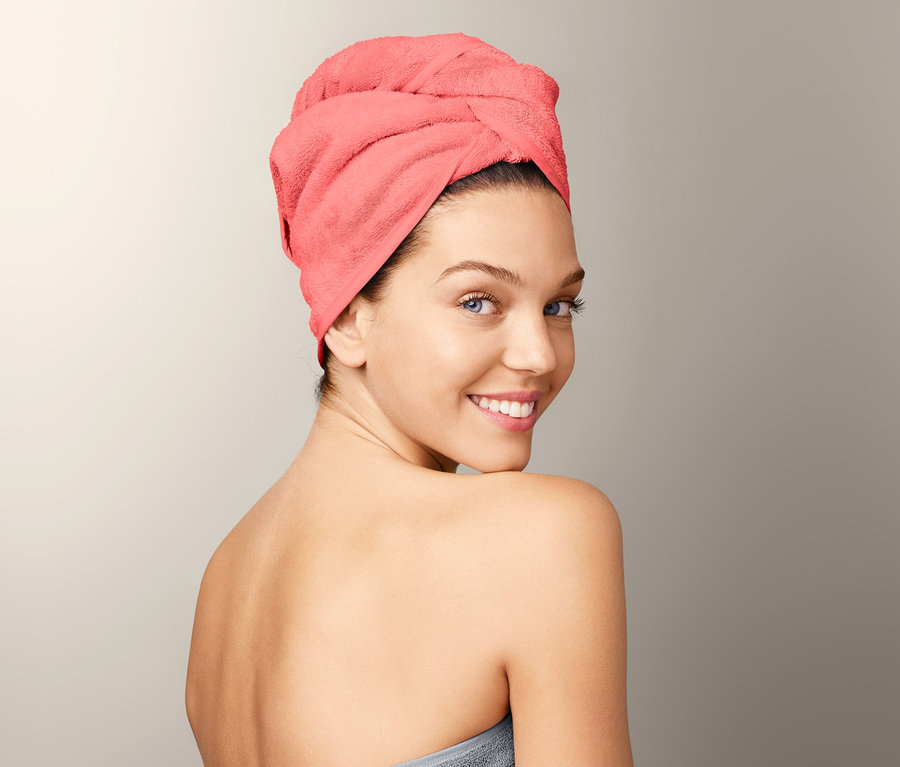 Žena sa usmieva cez plece, má na sebe uterákový turban a je zabalená v sivej osuške.