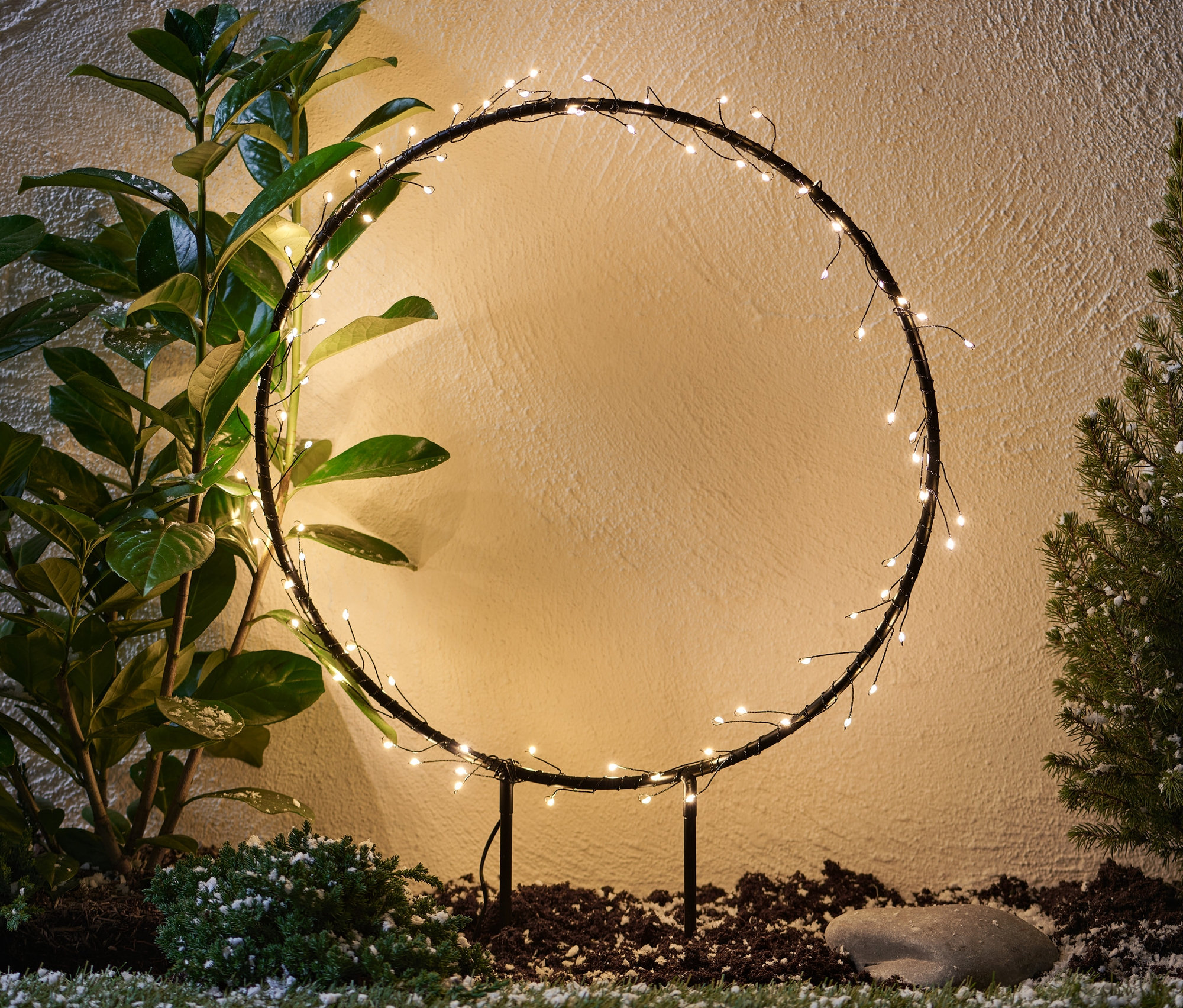 Kovový kruh s LED diódami do exteriéru stojí medzi rastlinami.