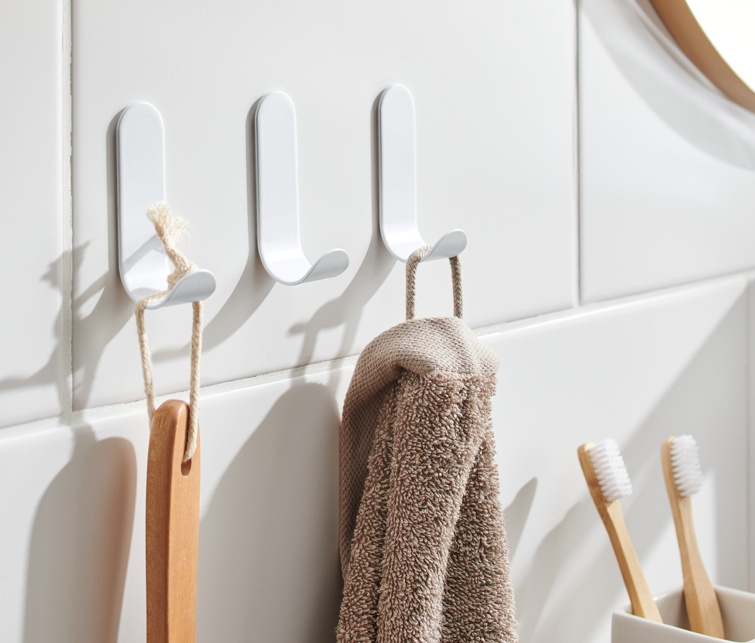 Na bielych dlaždiciach visia tri samolepiace háčiky, na ktorých visí kefa a uterák.