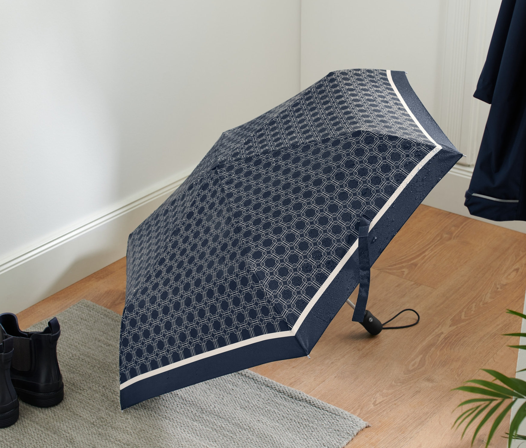 Otvorený automatický skladací dáždnik s geometrickým vzorom leží na podlahe vedľa topánok.