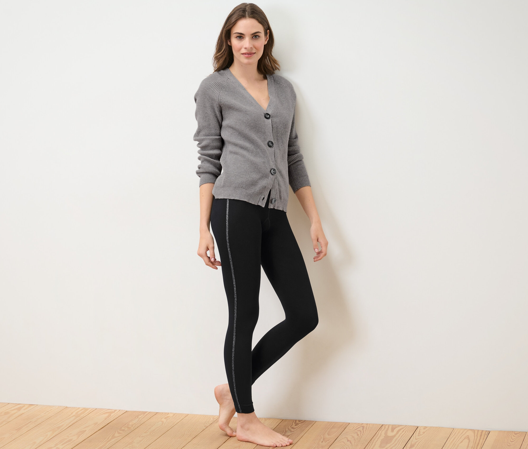 Žena pózuje v termolegínsach s trblietavým lemom a sivom svetri.