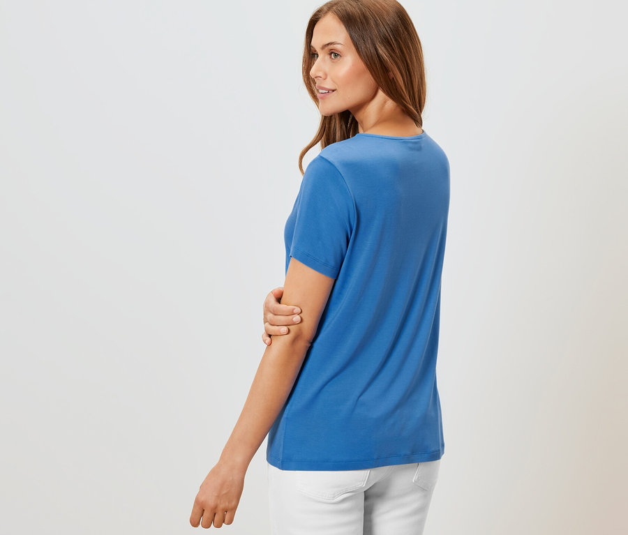 Žena pózuje v kobaltovomodrom tričku so záhybom a bielych nohaviciach.