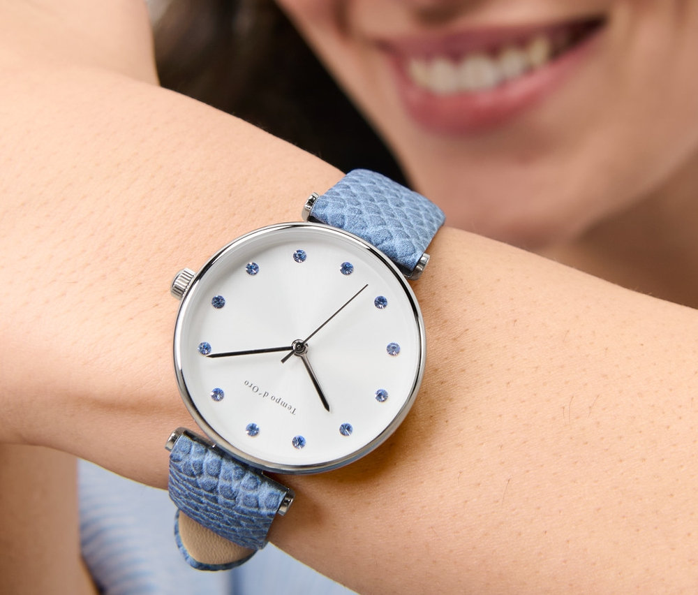 Usmievajúca sa žena má na zápästí náramkové hodinky s koženým remienkom a kryštálmi.
