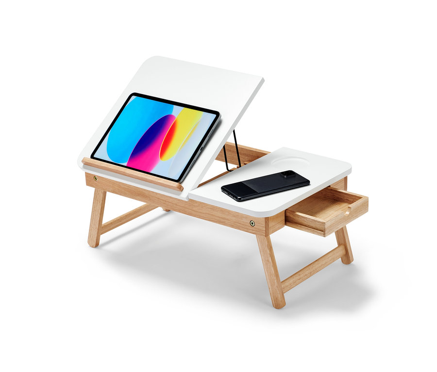 Biely stolík do postele na notebooky so svetlohnedými nohami. Na stolíku je tablet a mobilný telefón.