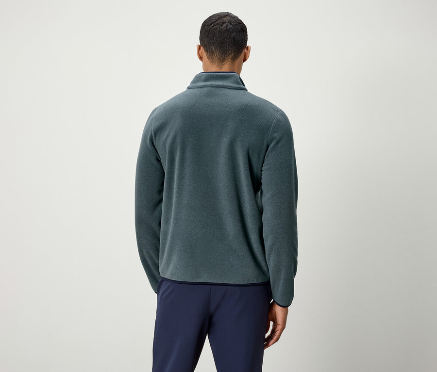 Muž chrbtom k fotoaparátu má na sebe zelenú fleecovú bundu a modré nohavice.