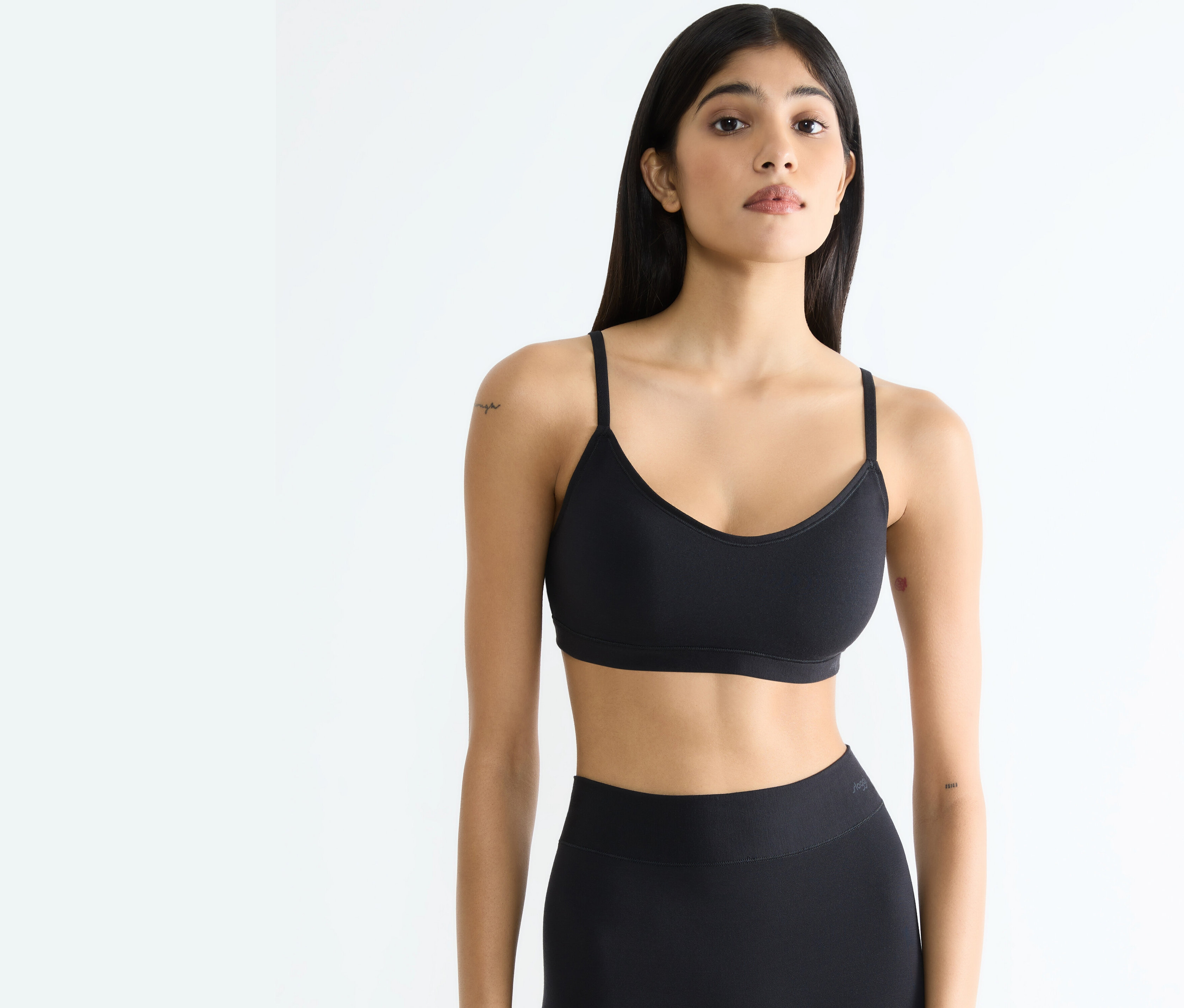 Žena v čiernom športovom tope a legínach pózuje na bielom pozadí.