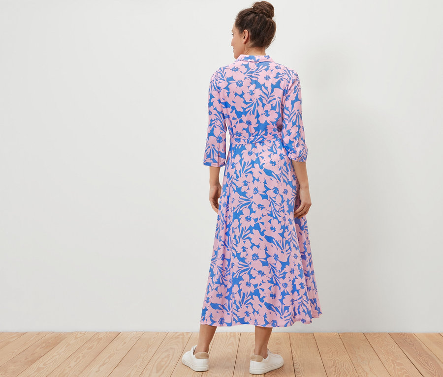 Žena chrbtom k fotoaparátu má na sebe košeľové šaty s potlačou.