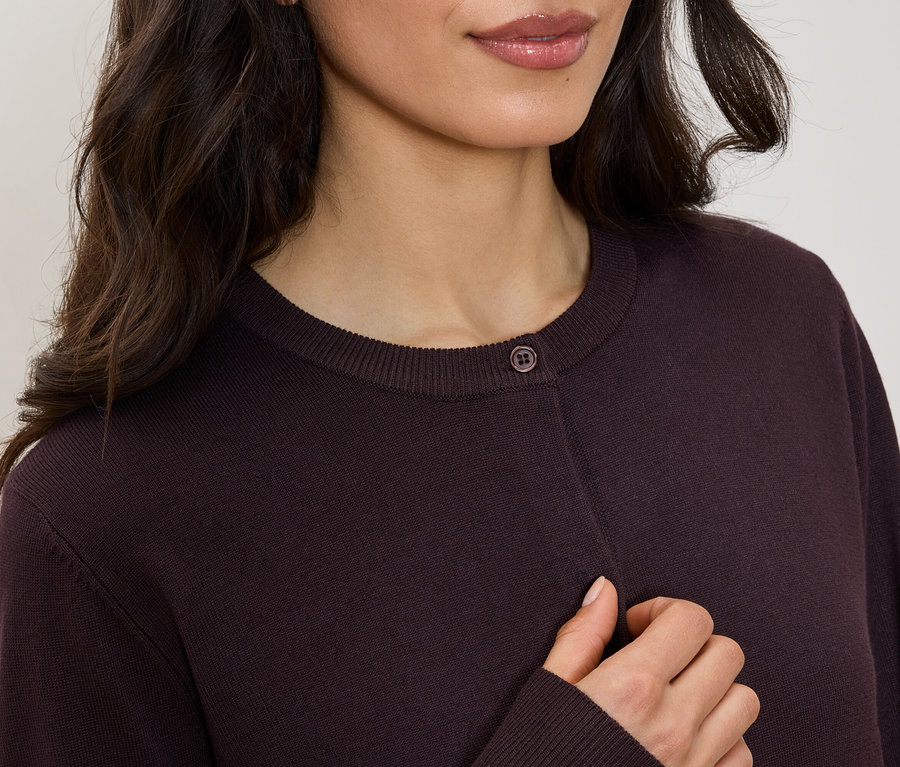 Horná časť tela ženy v bordovom svetri s okrúhlym výstrihom a jedným gombíkom.