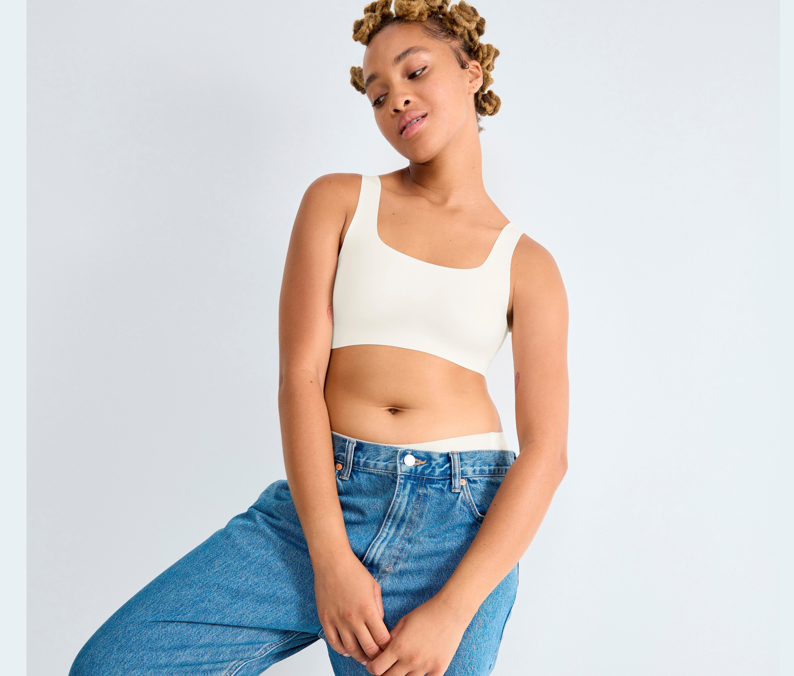 Mladá žena pózuje v džínsových nohaviciach a tope Sloggi ZERO Feel 2.0 v hodvábnej bielej farbe.